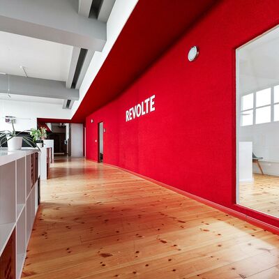 weißes Arbeitsplatzregal, rote Teppichwand, darin Fenster zum Meetingraum