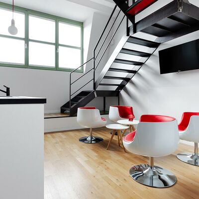 Lounge mit weiß-roten Designer-Sesseln unter grauer Treppe, Bildschirm, großes Fenster